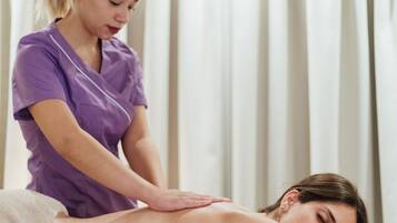 A person receiving a massage in a room with a bed and curtains.