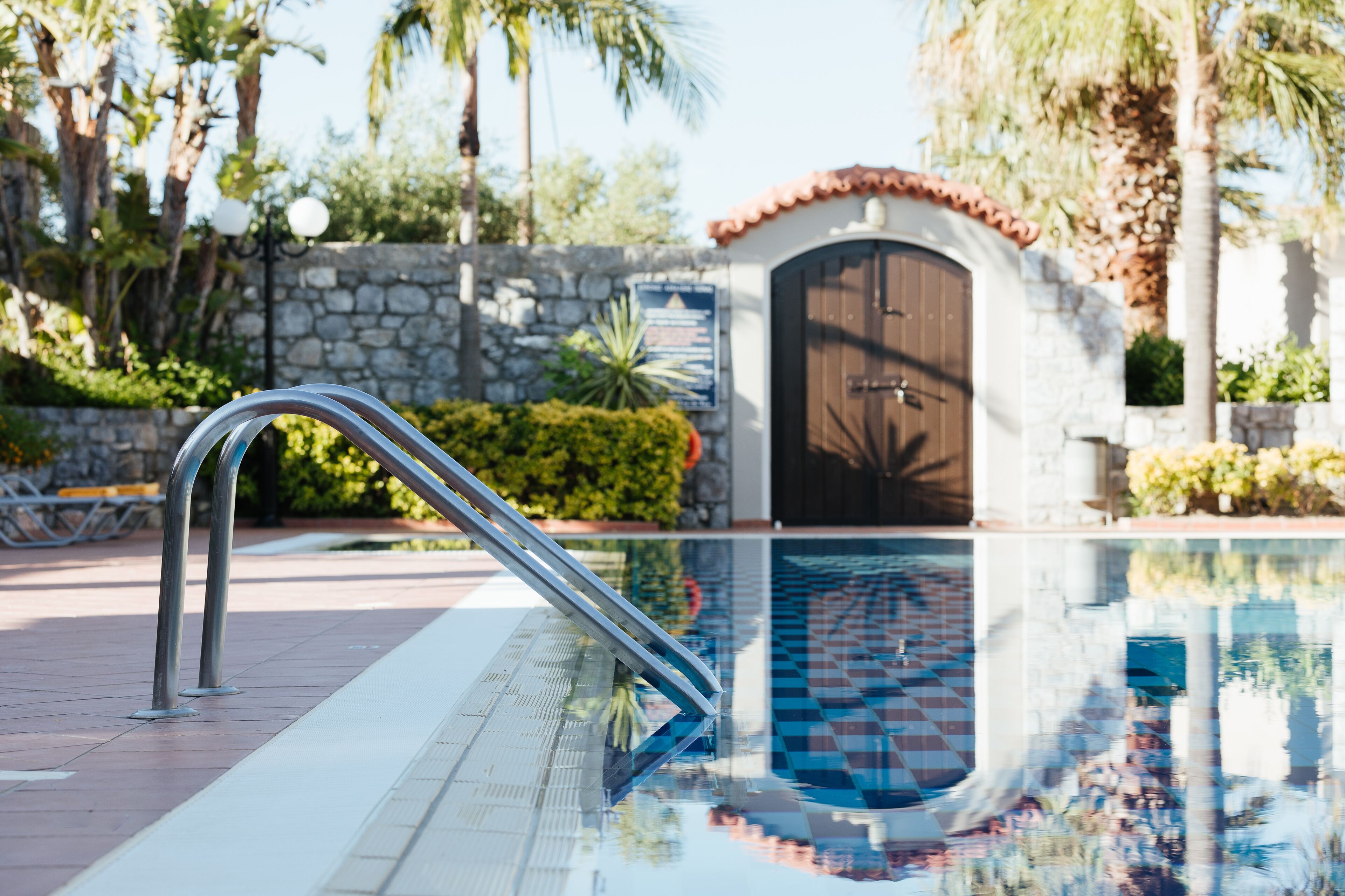 Una piscina con barandilla de metal, pared de piedra y puerta con techo de tejas.