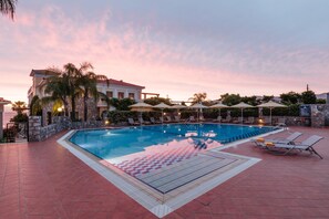 A swimming pool with lounge chairs and umbrellas, surrounded by stone walls and palm trees. - Akti Taygetos Conference Resort (Kalamata)