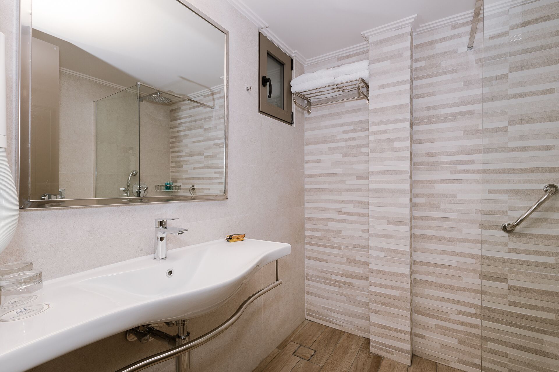 A bathroom with a white sink, a mirror, a shower with a glass door, and a towel rack.