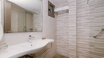 A bathroom with a white sink, a mirror, a shower with a glass door, and a towel rack.