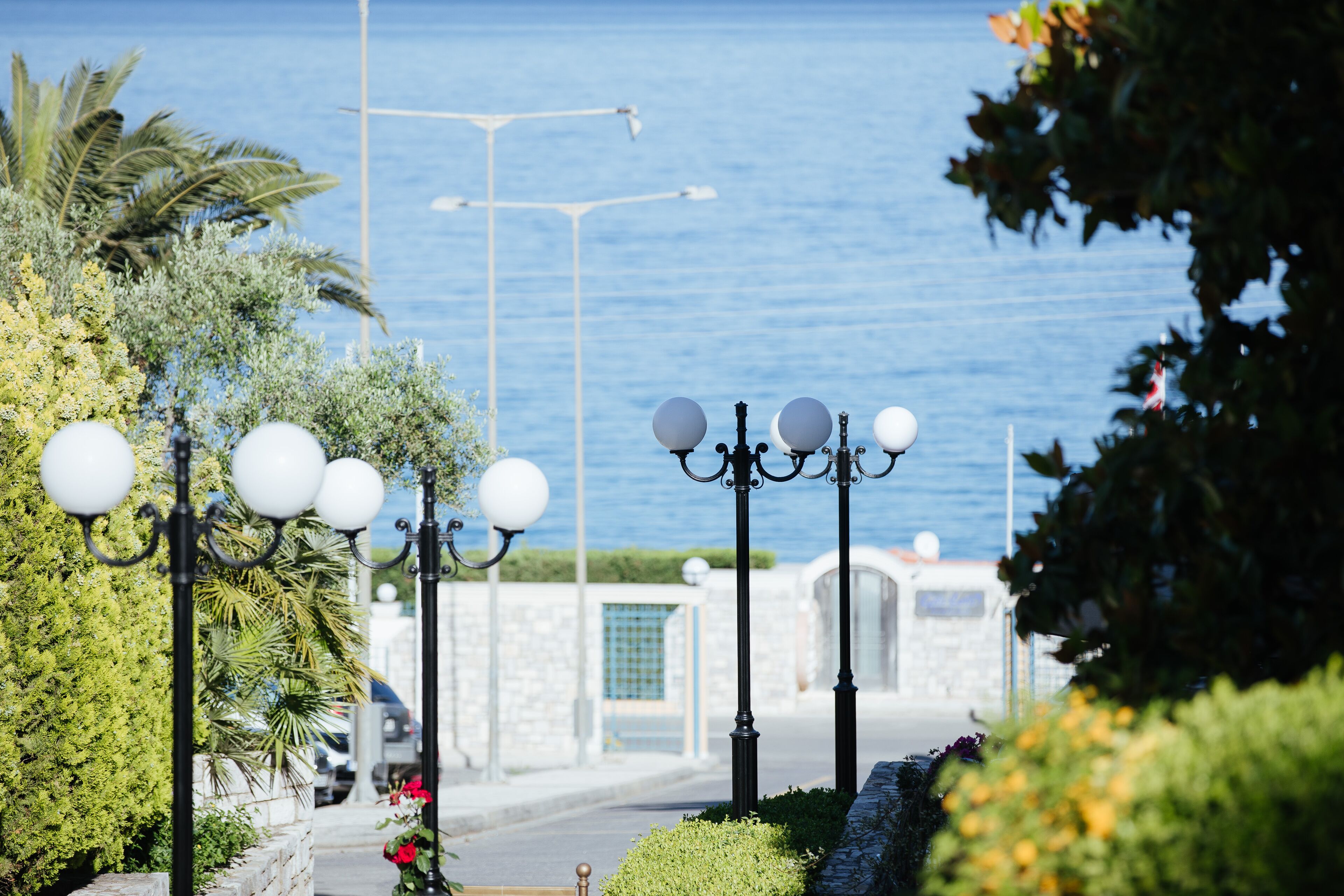 A coastal street with street lamps, a stone wall, and a view of the sea.