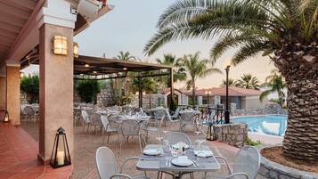 An outdoor dining area with tables and chairs, a pool, and palm trees.