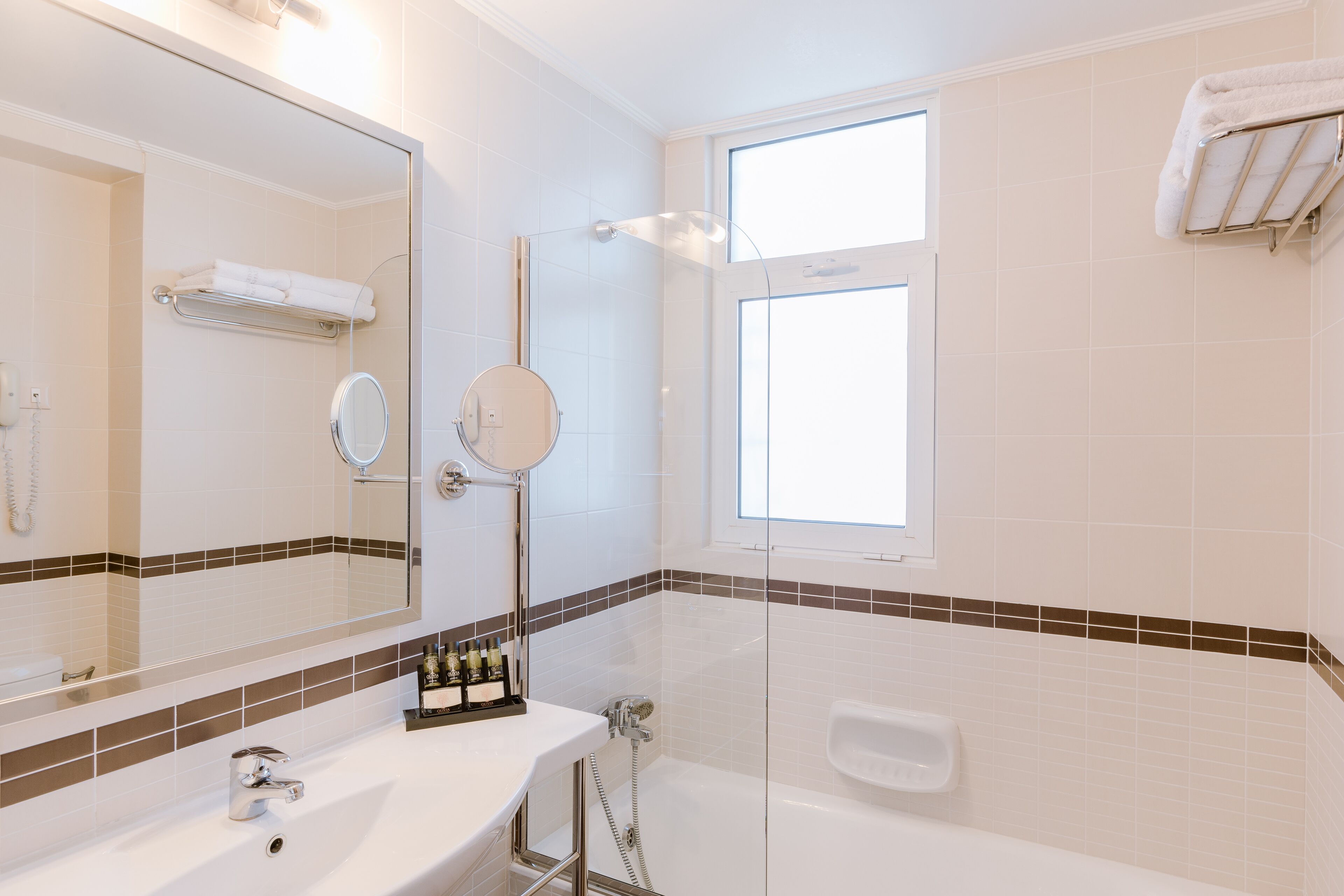 A modern bathroom with a large mirror, a glass-enclosed shower, and a window providing natural light.