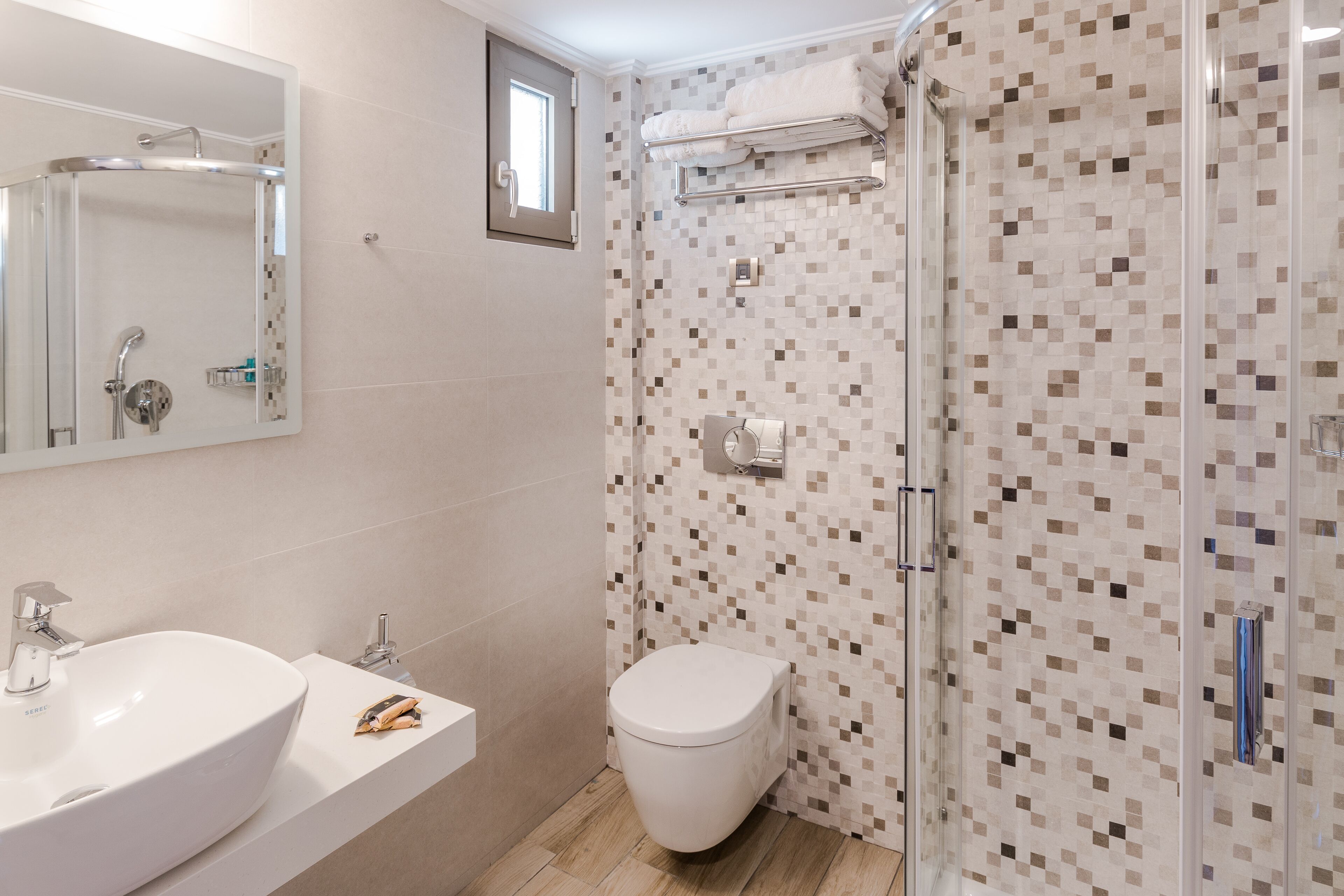 A bathroom with a large mirror, a sink, a toilet, and a shower area with a tiled wall.