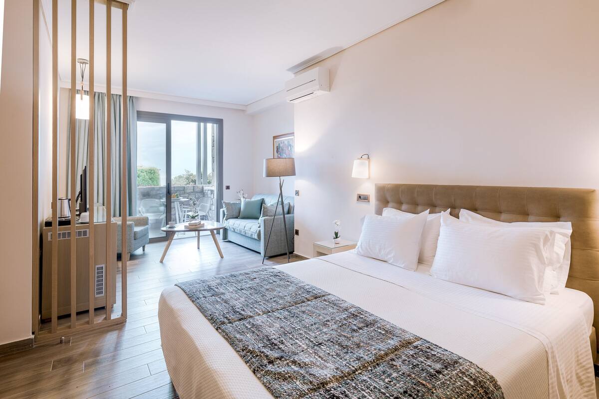 Et hotelværelse med en stor seng, en balkon med en sofa og udsigt til grønne områder.