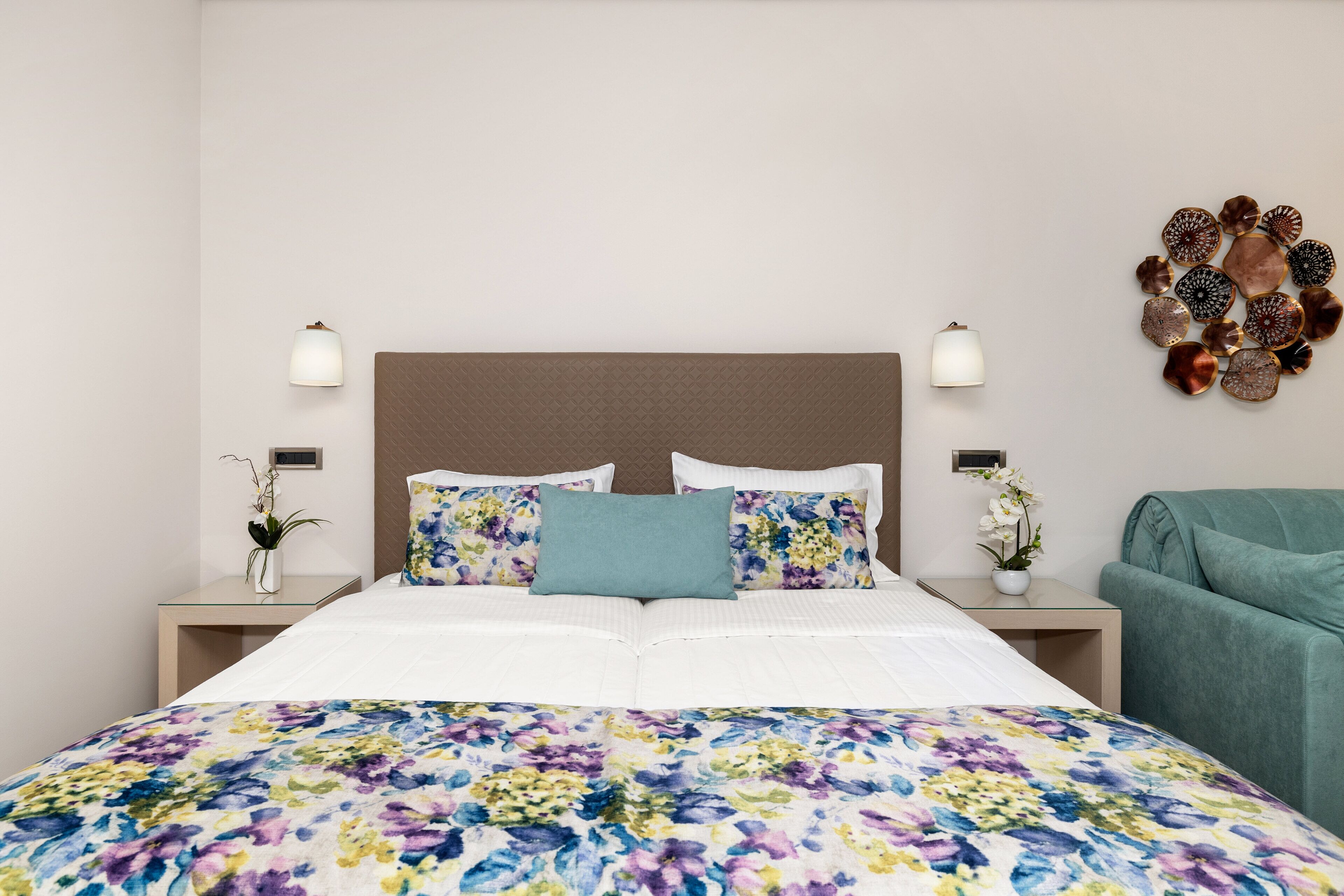 A hotel room with a large bed, two bedside tables, a green armchair, and a decorative wall piece.