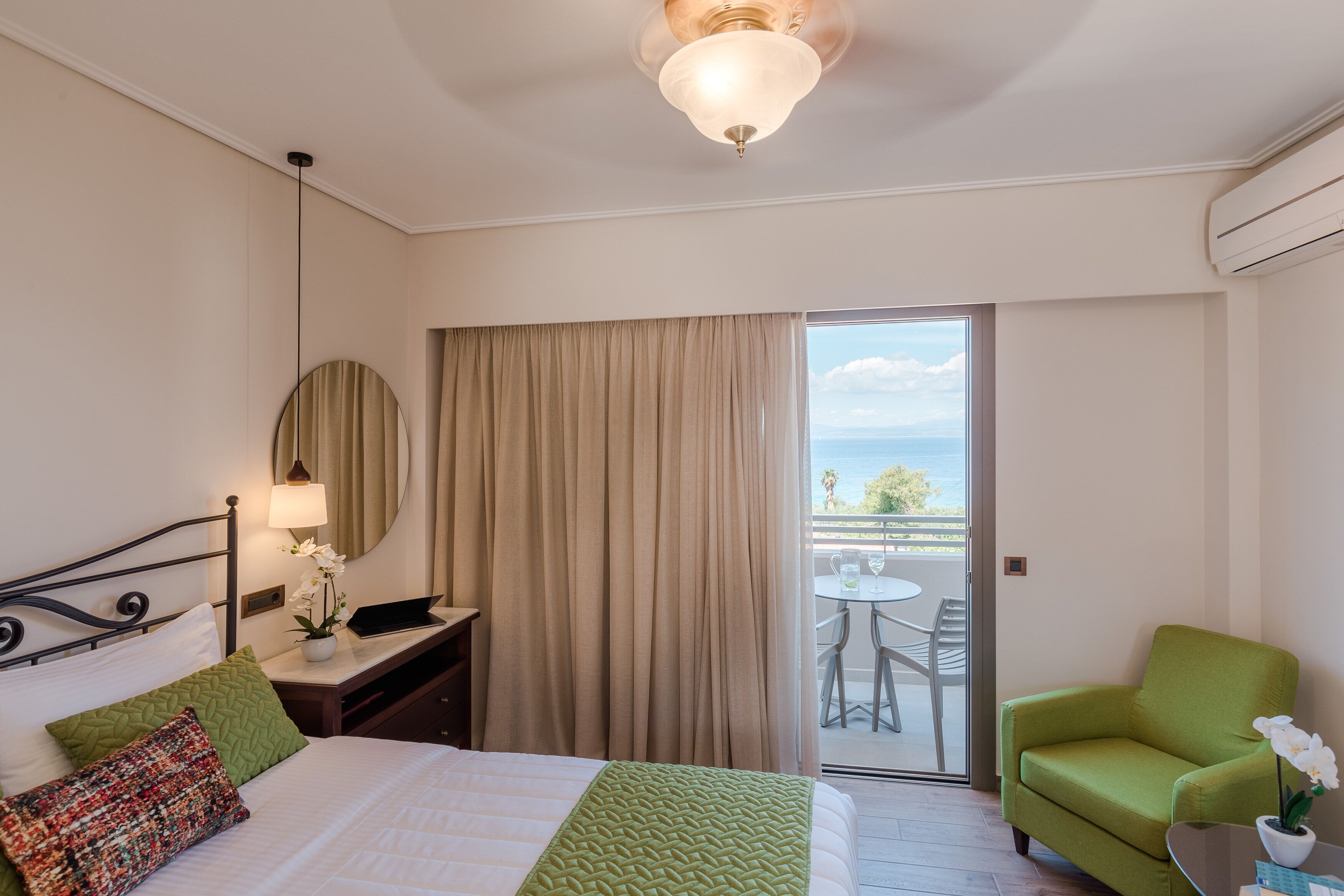 A hotel room with a bed, a desk, a laptop, a chair, and a balcony with a view.