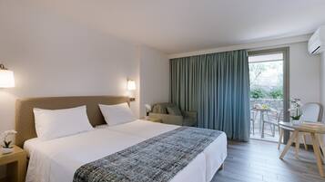 Una habitación de hotel con una cama grande, una mesita con una silla, un balcón con mesa y sillas, y un equipo de aire acondicionado.