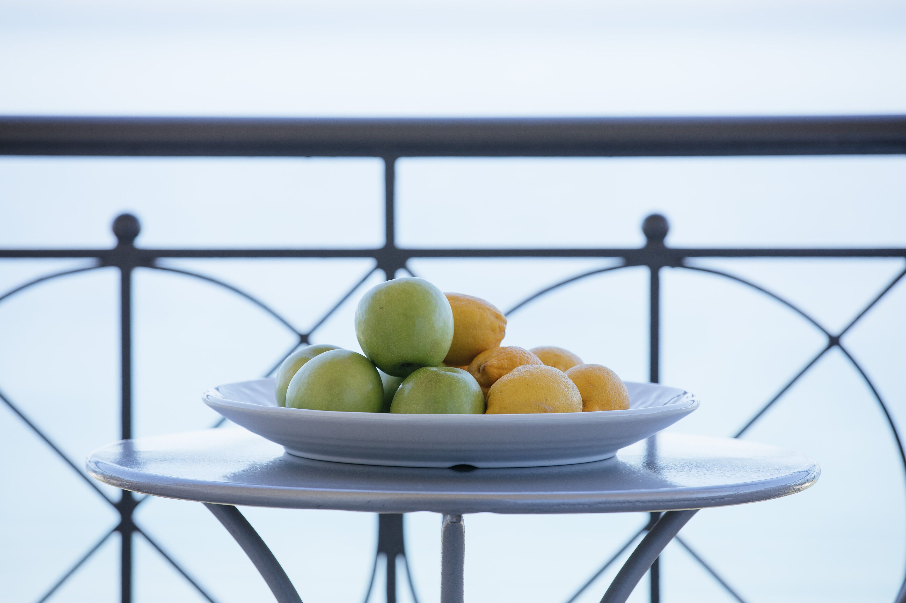Een bord met fruit op een tafel, met een metalen hekwerk op de achtergrond.