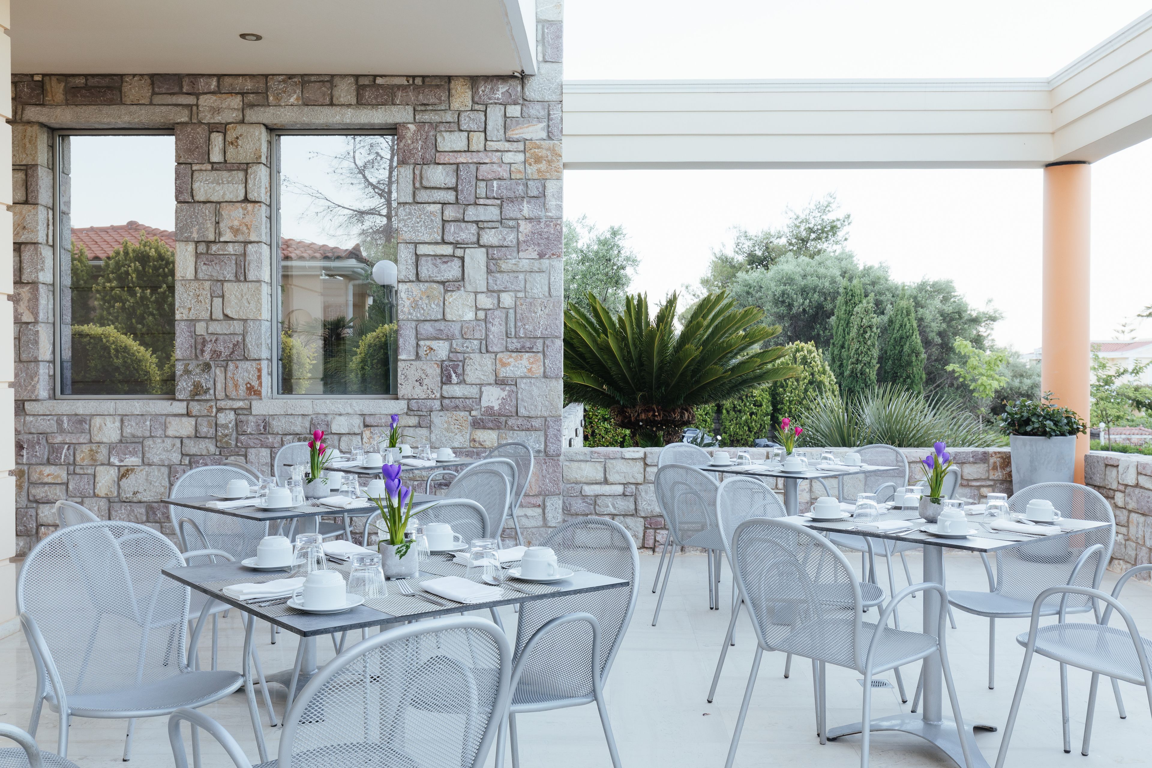 Un área de comedor al aire libre con paredes de piedra y sillas de metal, con mesas dispuestas para comer.