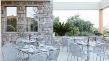 Un área de comedor al aire libre con paredes de piedra y sillas de metal, con mesas dispuestas para comer.