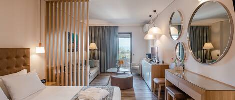 A modern hotel room with a large bed, a desk, a sofa, and a dining area.