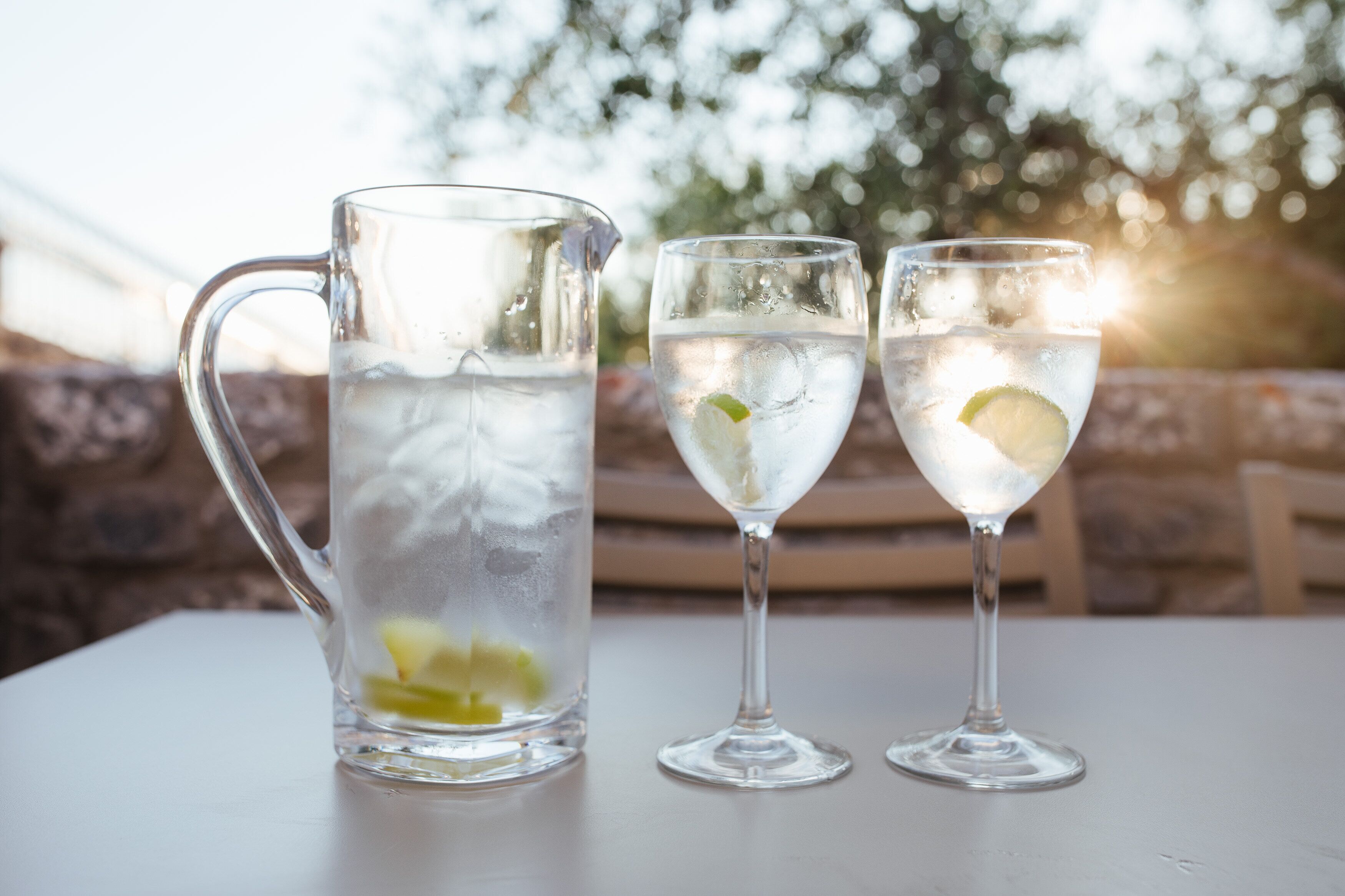 A pitcher and two glasses of water with lime slices on a table outdoors.