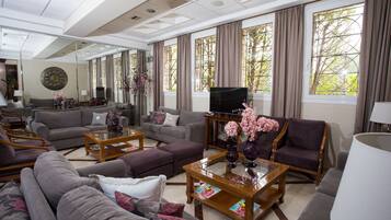 A spacious living room with multiple seating options, a flat-screen TV, and large windows with curtains.