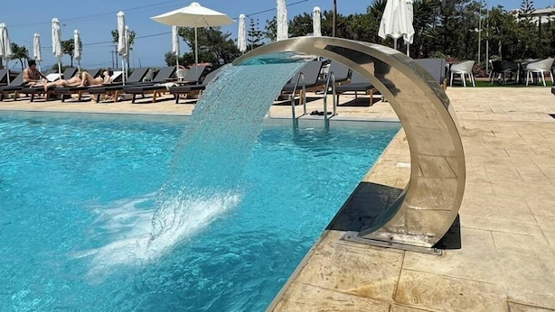 Une piscine dotée d’un élément décoratif aquatique aux formes arrondies, de chaises longues et de parasols.