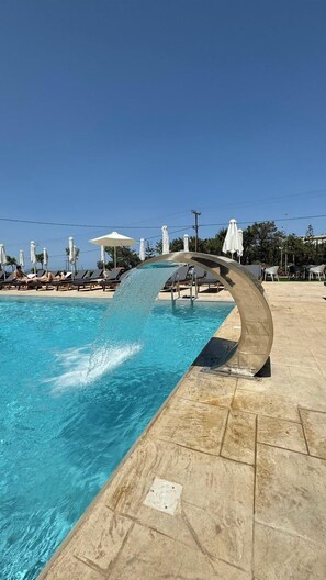 A swimming pool with a curved water feature, lounge chairs, and umbrellas. - Azul Eco Hotel (Rethymno)