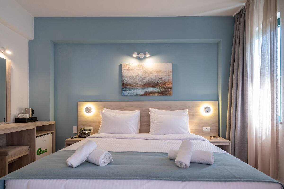 A hotel room with a bed, bedside tables, a desk, and a painting on the wall.