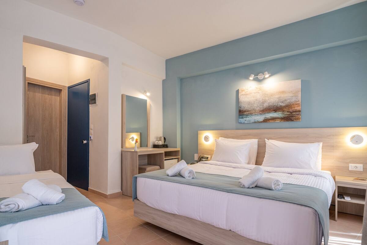 A hotel room with two beds, a desk, a chair, a mirror, a painting, and a nightstand with a lamp.