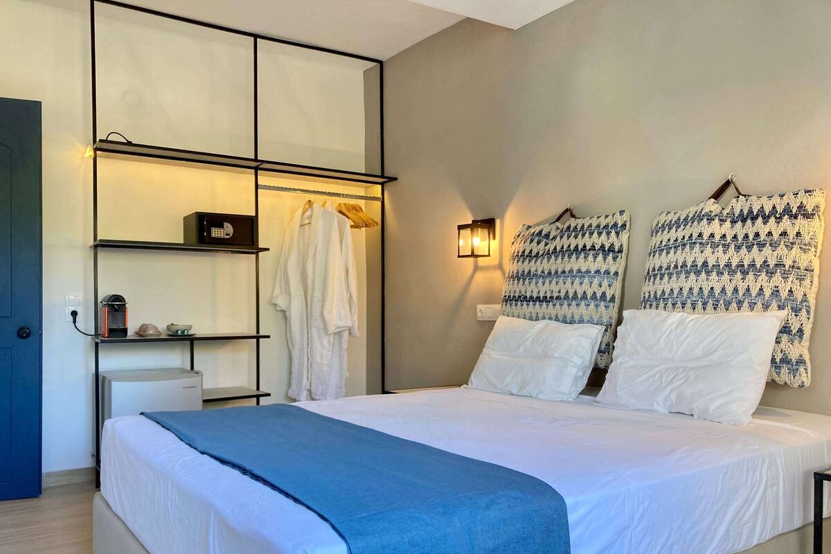 A bedroom with a bed, a wardrobe, a shelf with a kettle, and a wall-mounted lamp.