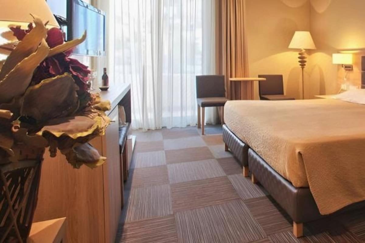 A hotel room with a large bed, bedside tables, a desk, a chair, and a TV.