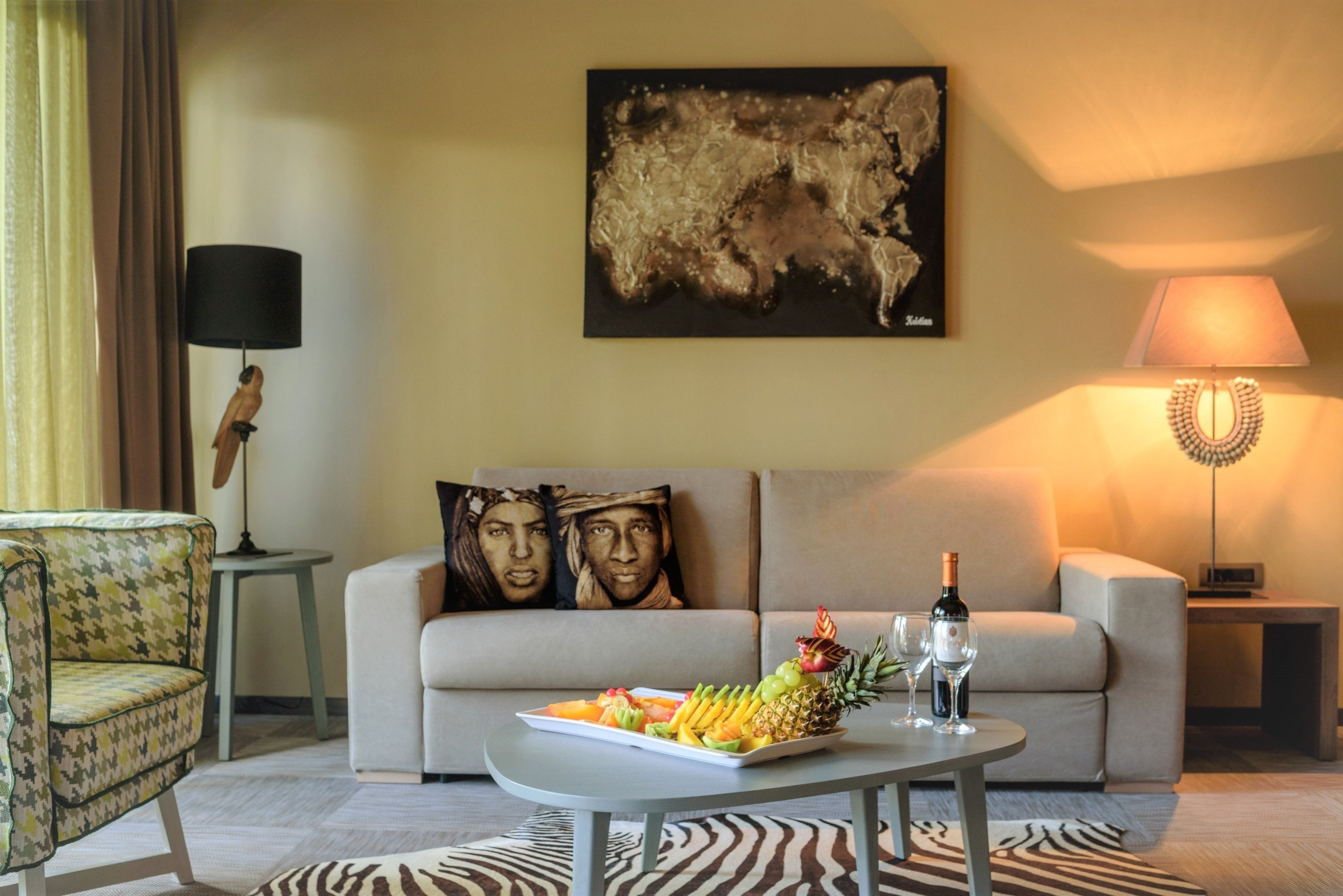 Uma sala de estar moderna com um sofá, uma mesa de centro com frutas e vinho, uma luminária e um quadro na parede.