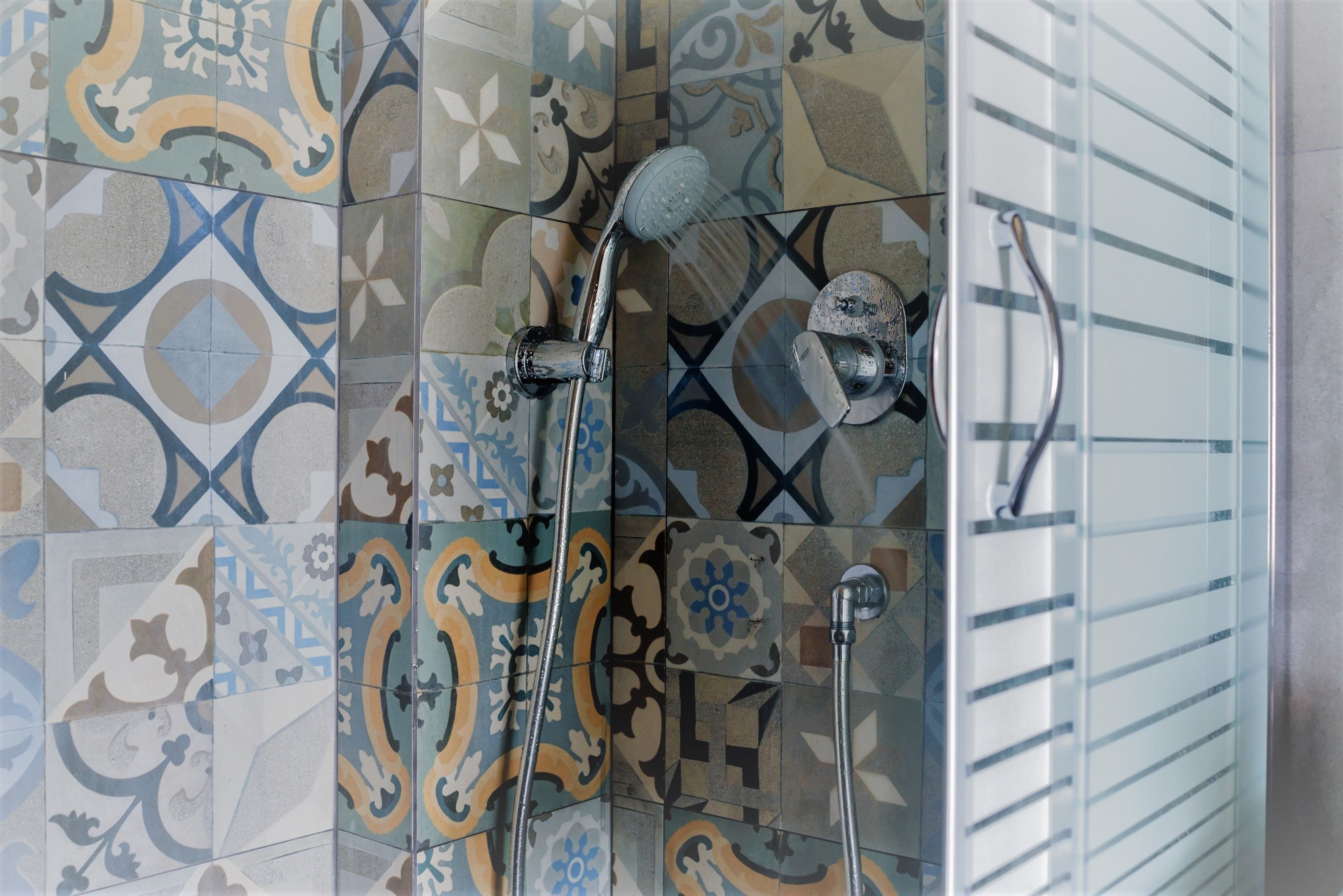 A shower with a rain showerhead and a handheld showerhead, set against a wall with patterned tiles.