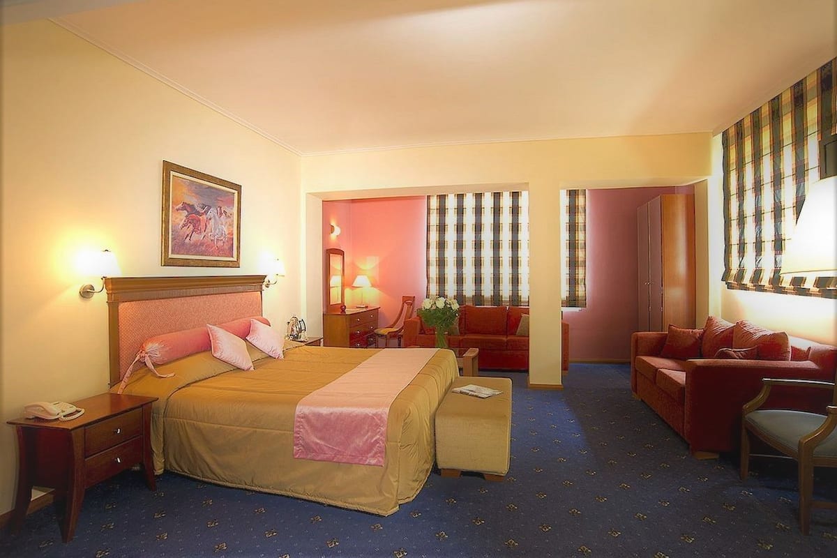 A hotel room with a large bed, bedside tables, a desk, a chair, and a sofa.