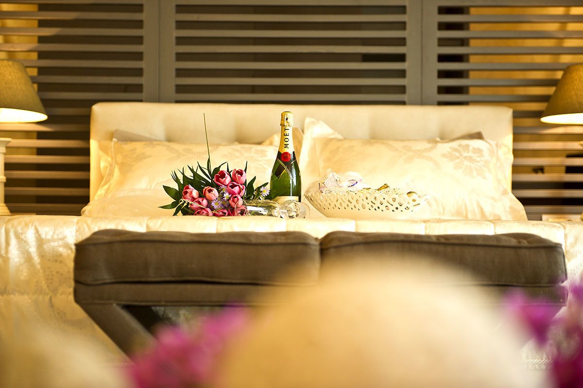 A bed with a bottle of champagne, a bouquet of flowers, and a decorative item on the pillows.