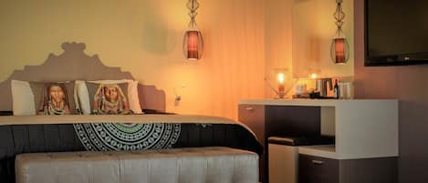 A modern bedroom with a large bed, bedside lamps, a TV, and a small desk area.
