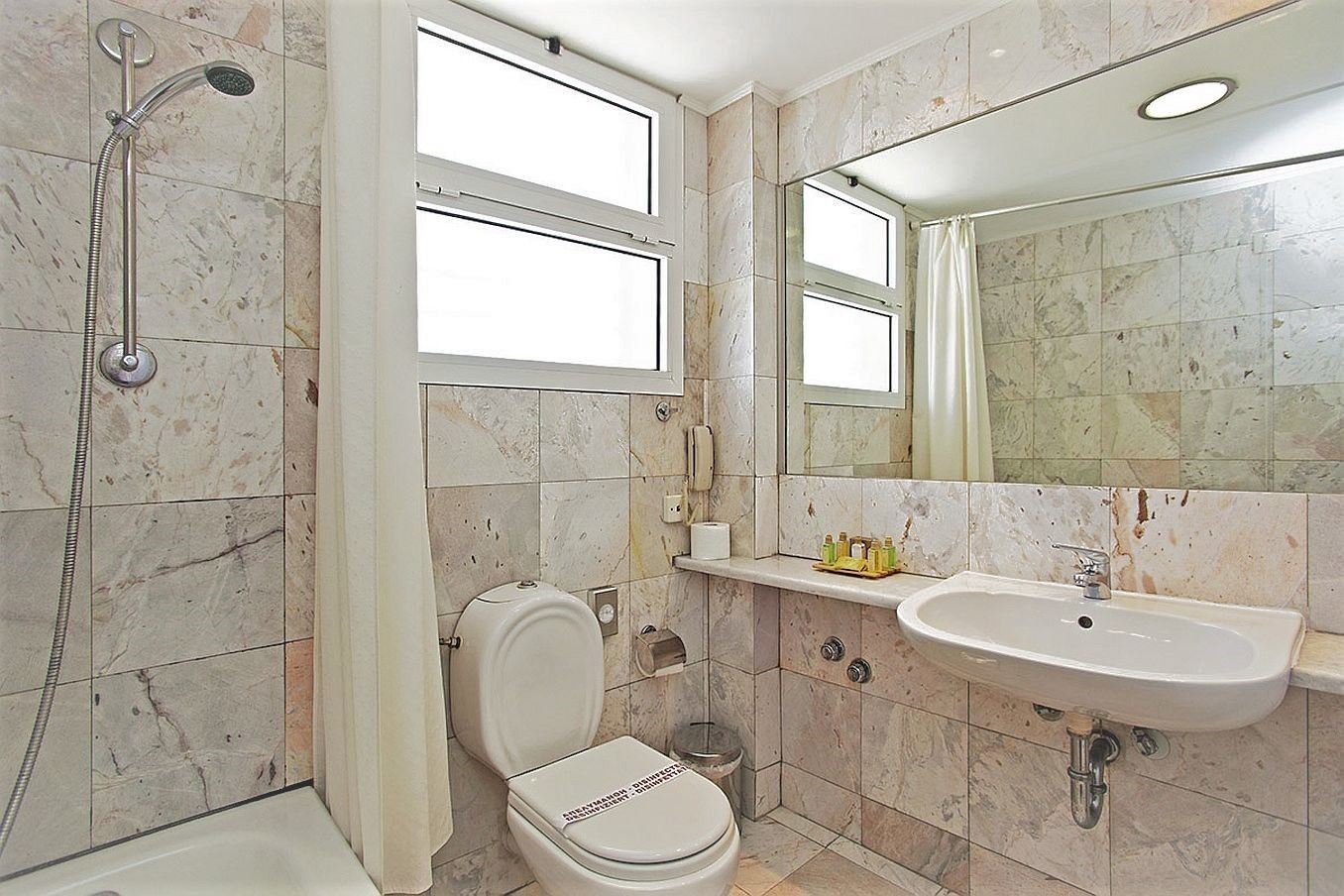 Un baño con ducha, inodoro, lavamanos y un espejo grande.