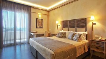 Habitación de hotel con una cama grande, lámparas de noche, un escritorio y vistas a través de cortinas translúcidas.