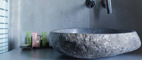 A stone basin sink with a modern faucet and soap dispensers on a countertop.