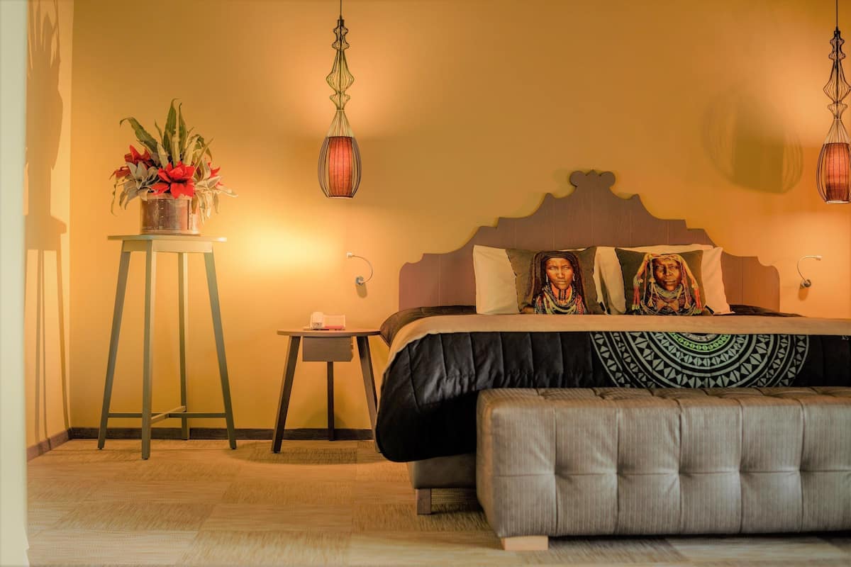A bedroom with a bed, bedside tables, a small stool, and a potted plant.