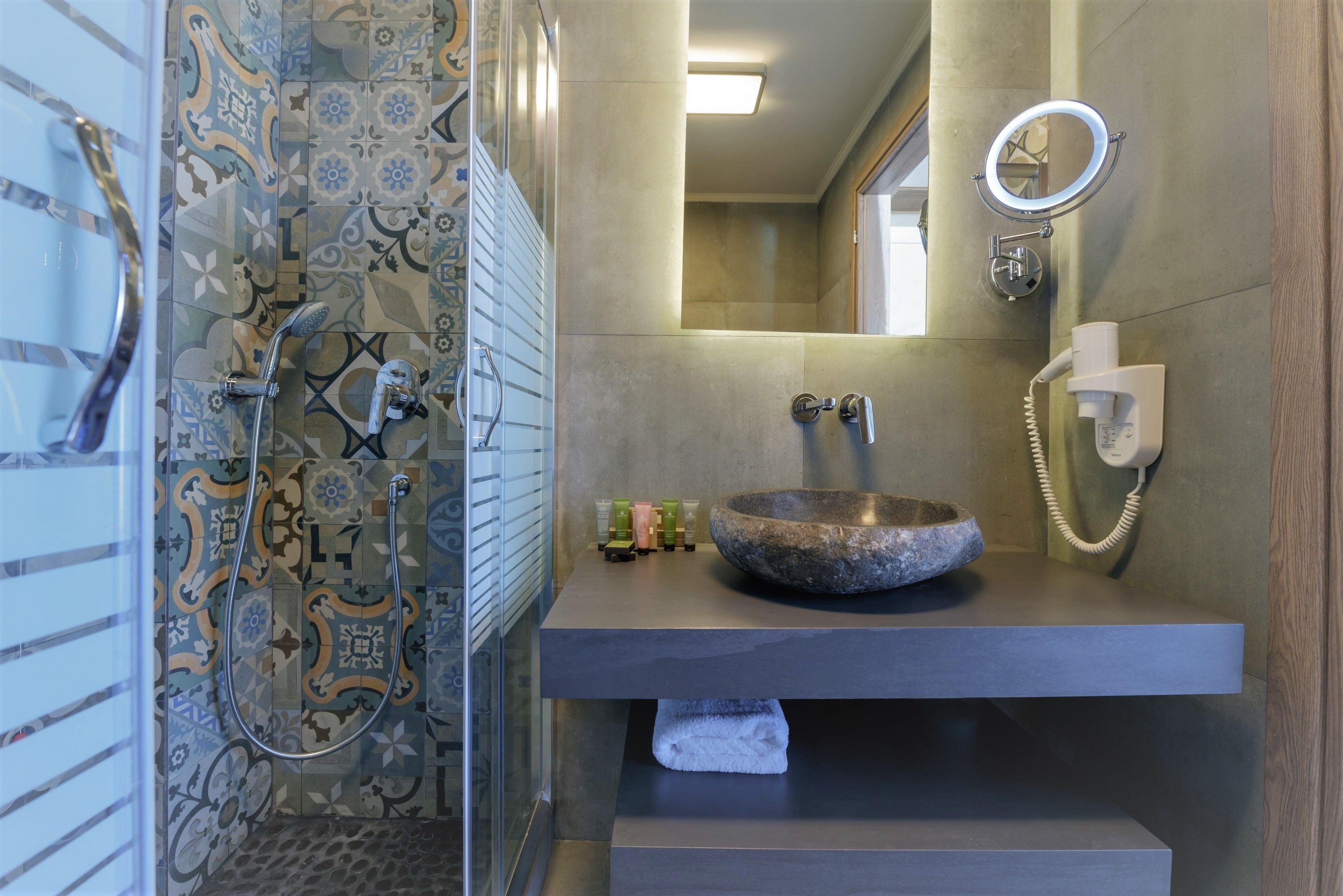 Un baño con ducha, un lavabo con cuenca de piedra, un espejo y un teléfono.