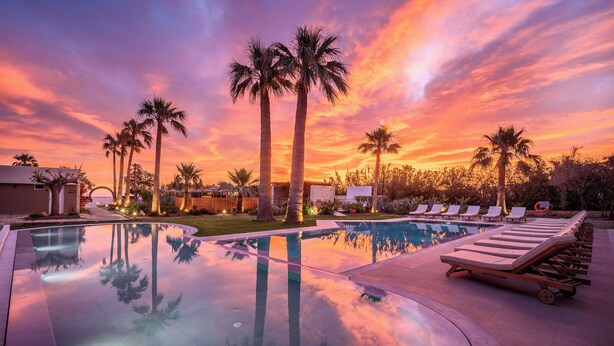 Una piscina con sillones de playa y palmeras al atardecer.