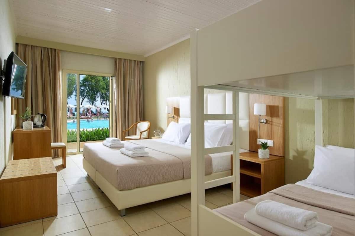 A hotel room with a bed, a desk, a chair, a TV, and a view of a pool.