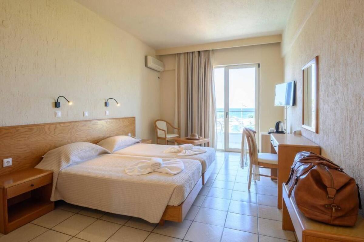 A hotel room with two beds, a desk, a chair, a TV, and a view of the sea.
