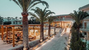 Un patio con palmeras, mesas al aire libre y un edificio con paredes de vidrio.