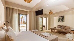 Habitación de hotel con una cama grande, un sofá, un televisor y un balcón con vistas a palmeras.