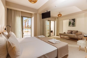 A hotel room with a large bed, a sofa, a TV, and a balcony with a view of palm trees. - Malia Bay Beach Hotel & Bungalows (Hersonissos)