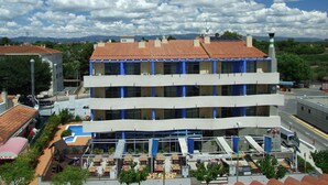 Un edificio de varios pisos con techo de tejas rojas, columnas azules y una zona de piscina con mobiliario exterior.