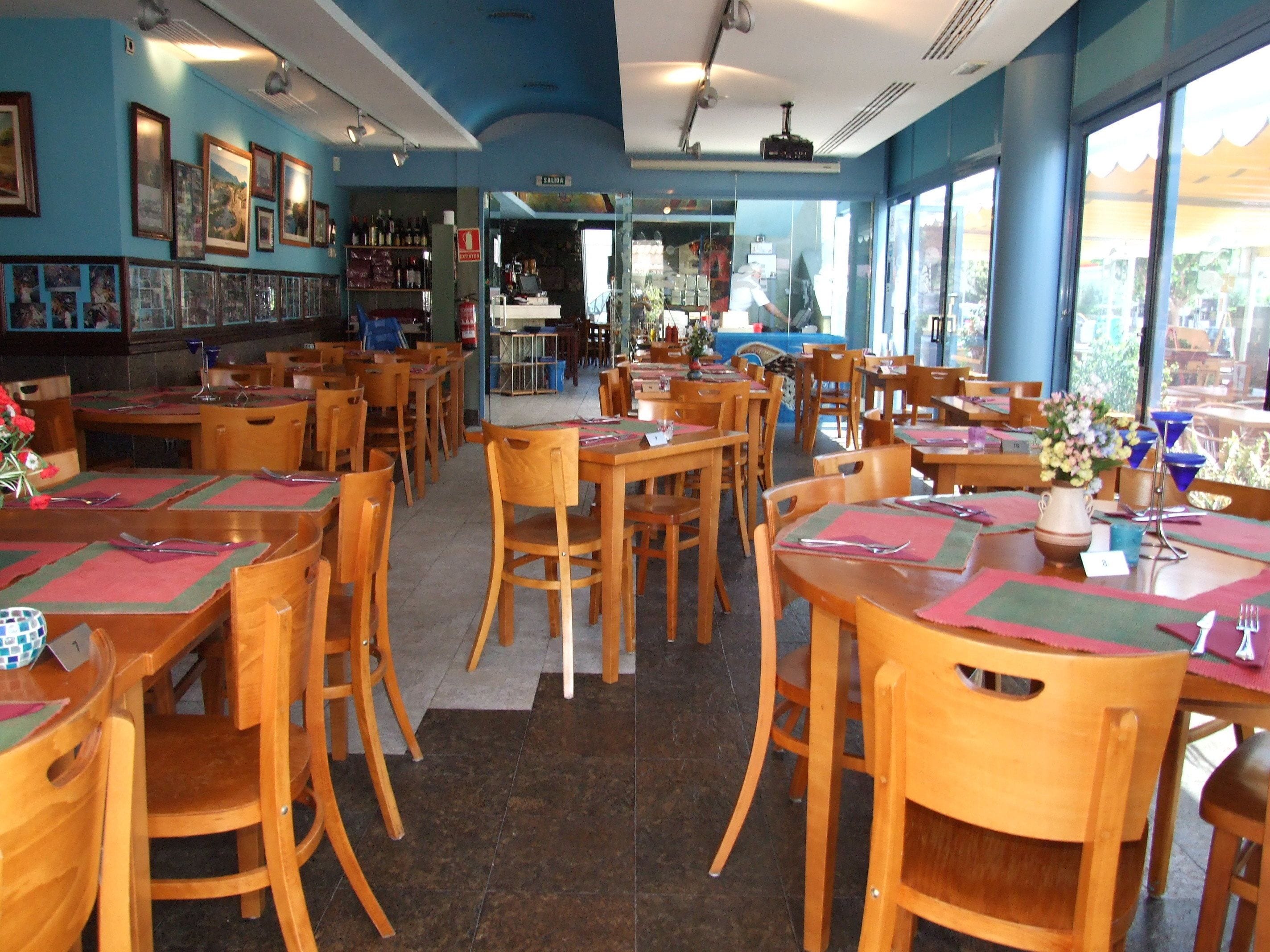 A restaurant with wooden tables and chairs, a bar area, and large windows.