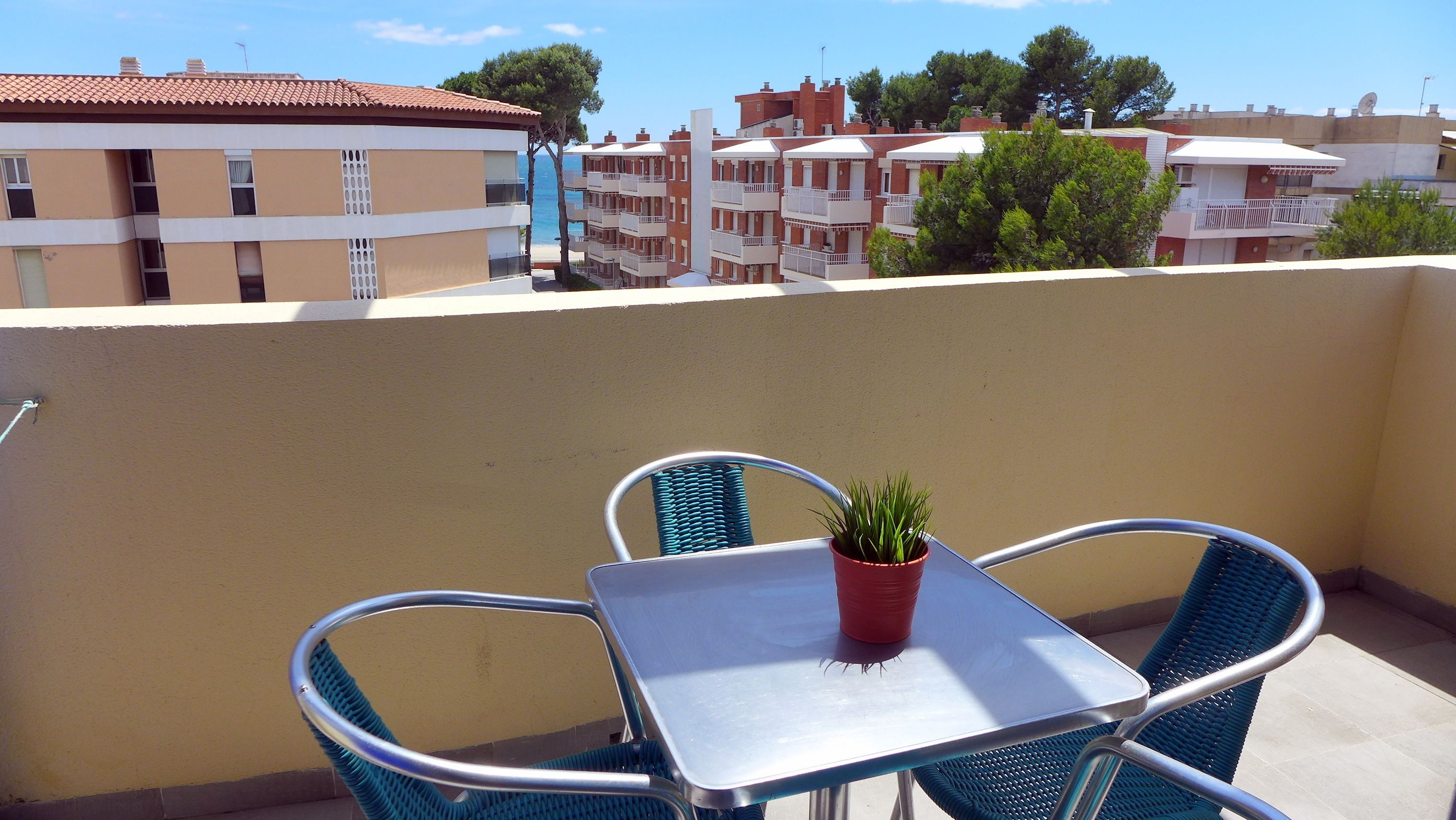 En balkon med et bord og stole, en potteplante og udsigt til boligbygninger.