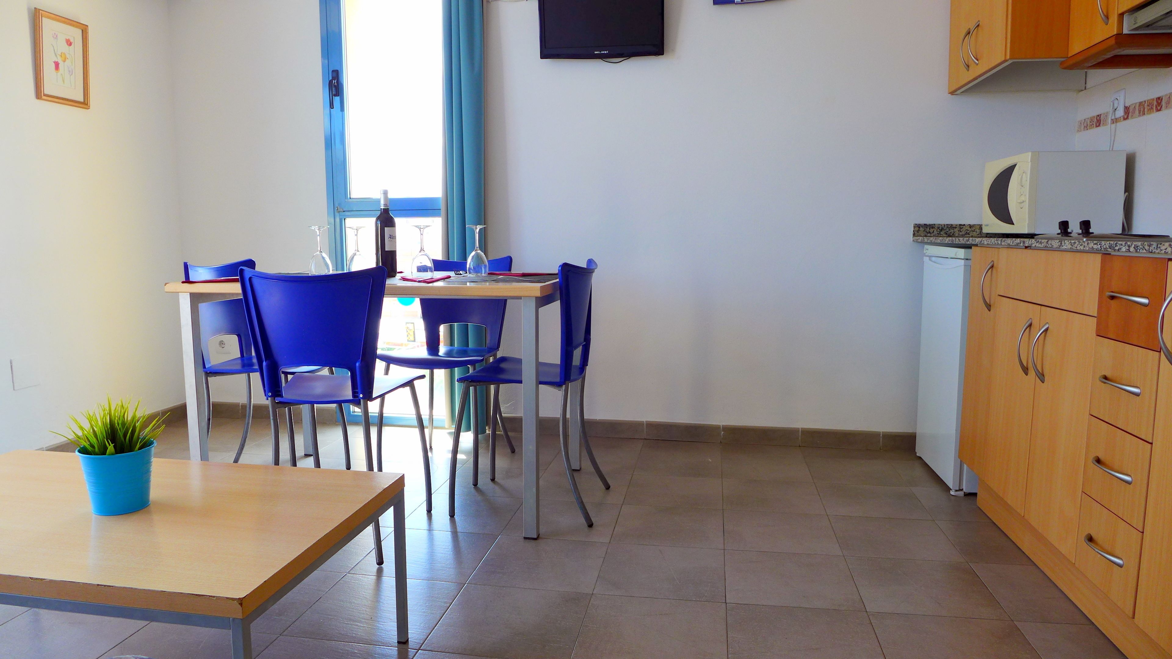 A small kitchen with a dining table and chairs, a microwave, and a TV mounted on the wall.