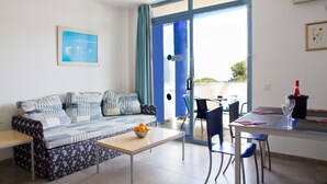 Una sala de estar moderna con un sofá, una mesa de comedor y sillas. Hay una ventana con cortinas azules, un cuadro enmarcado en la pared y un frutero sobre la mesa.