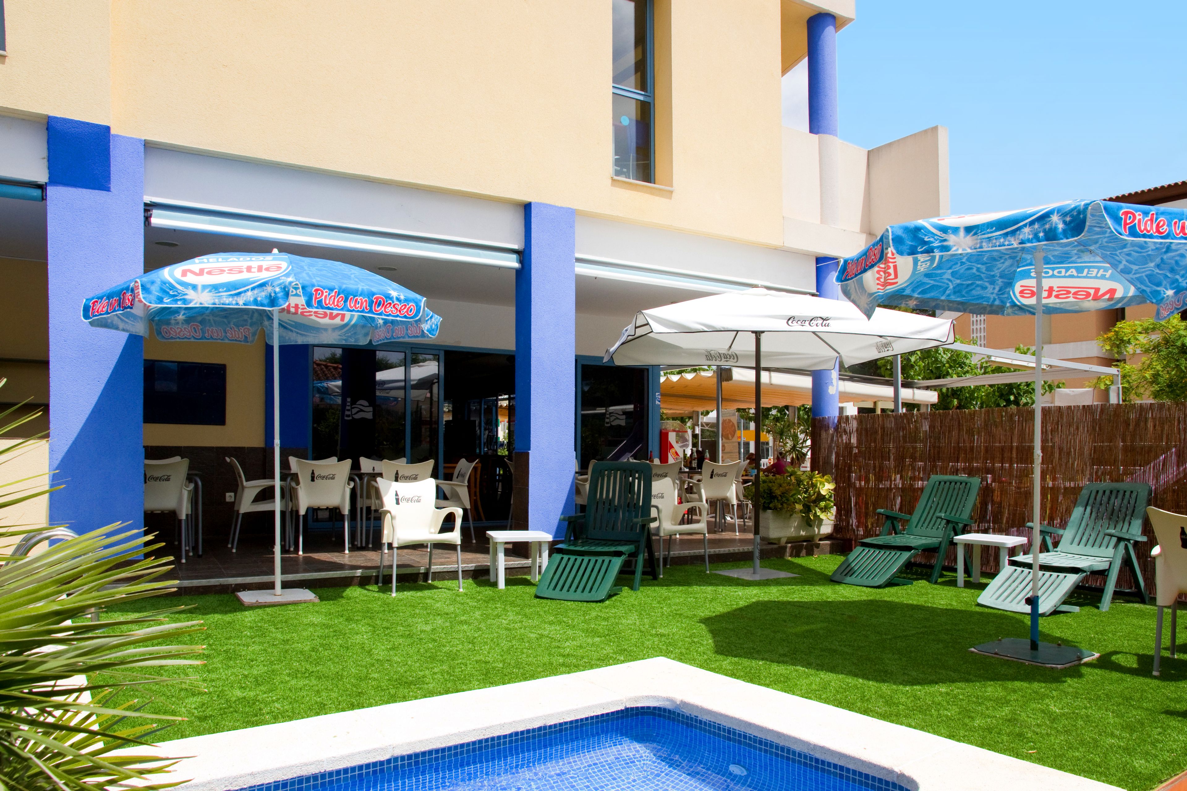 A pool area with artificial grass, lounge chairs, and umbrellas.