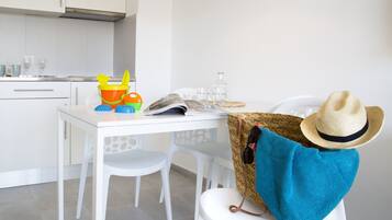 Una cocina con armarios blancos, encimera blanca y una mesa de comedor con sillas. Hay un sombrero y un bolso tejido en la silla.