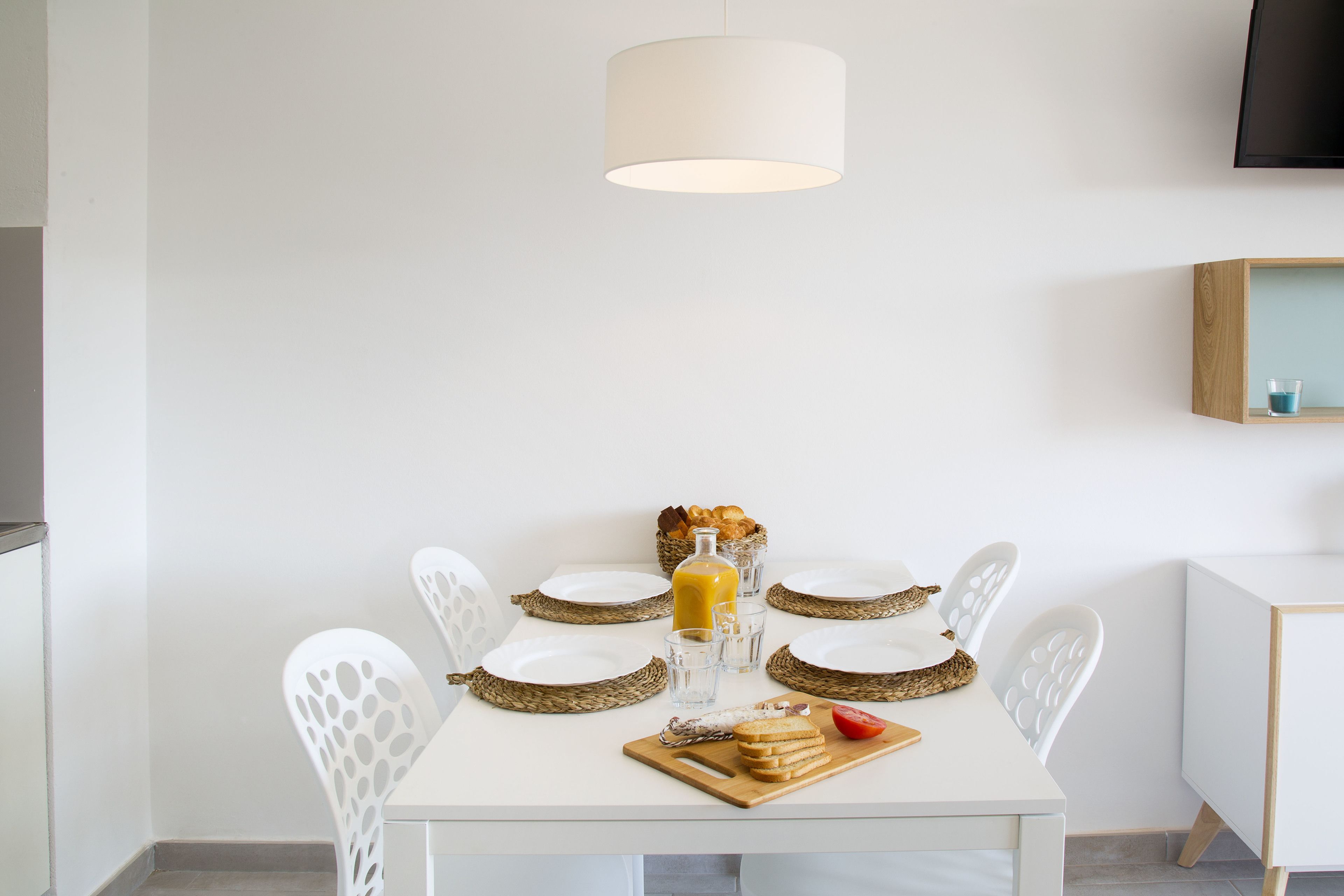 A dining table with white chairs, a white tablecloth, and a basket of bread.