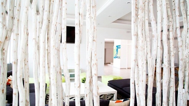 A modern living room with a black sofa, white coffee table, and a view of a kitchen area through a white curtain with a natural pattern. - RVApartaments Estartit Confort (Torroella de Montgrí)